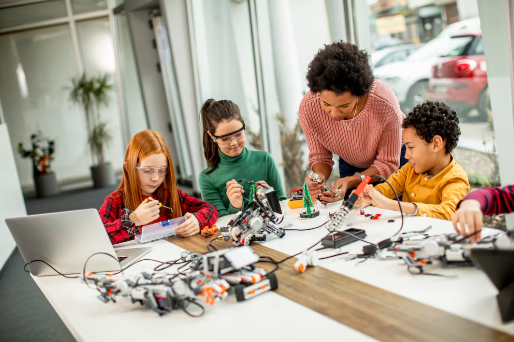 Students building and programming robots with a teacher in a STEM lab using laptops and electronic components.