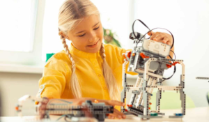 A young girl in a yellow shirt building a robot in a STEM lab.