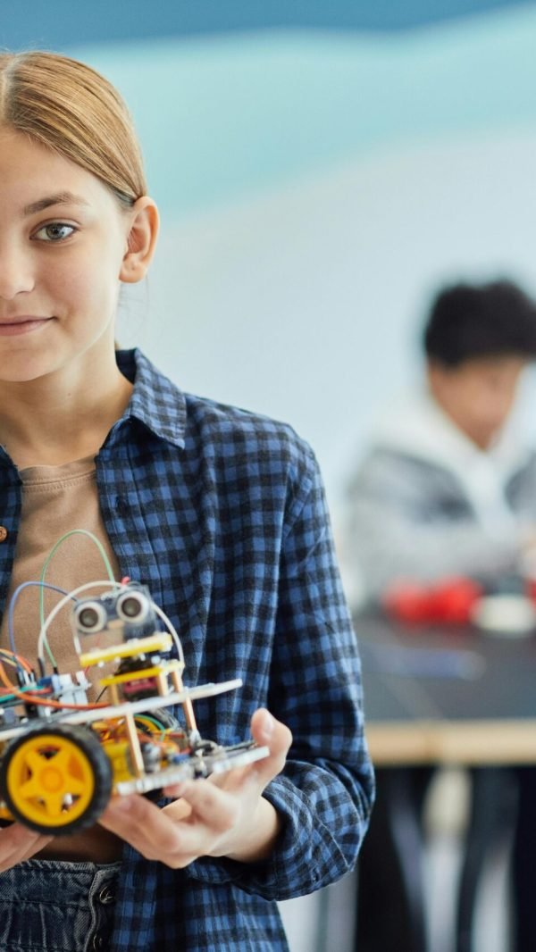 Girl proudly displays her robotics project in a classroom setting.