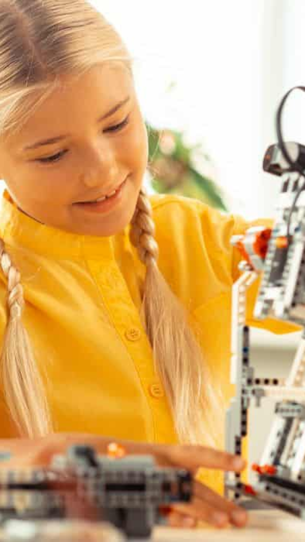 A young girl in a yellow shirt building a robot in a STEM lab.